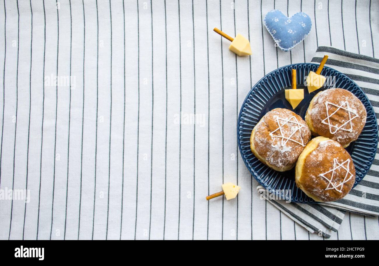 Bonne Hanoukkah.Un régal traditionnel de beignets avec David star et dreidel fait à partir de fromage et de bâtonnets de biscuit.Décoration coeur en tissu bleu.Copier l'espace. Banque D'Images