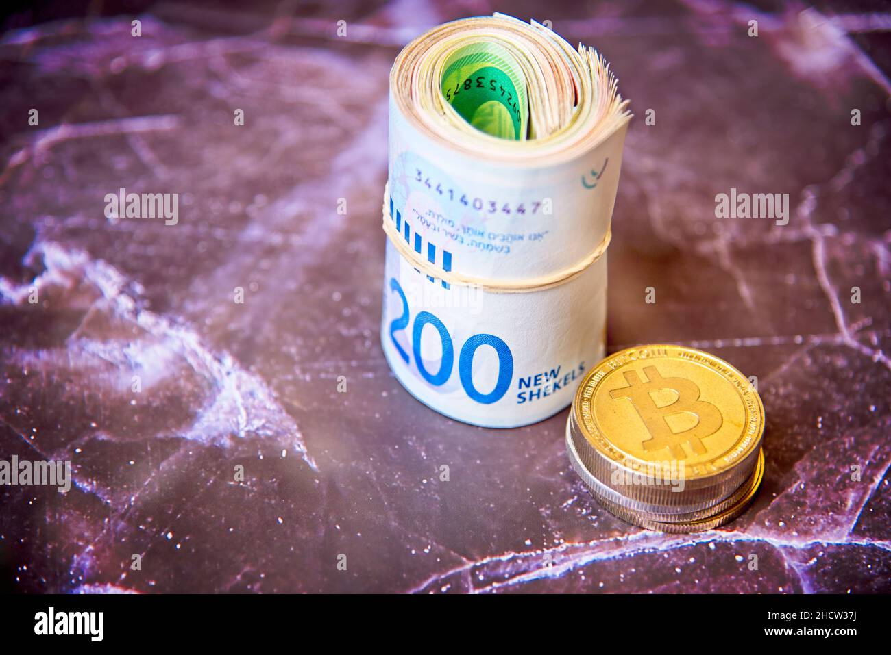 Rouler les billets israéliens Shekel ils près des jetons de crypto-monnaie bitcoins pièces de bits, vu d'en haut, sur un vieux panneau de marbre.Mise au point sélective. Avec espace pour le placement du texte.Photo de haute qualité Banque D'Images