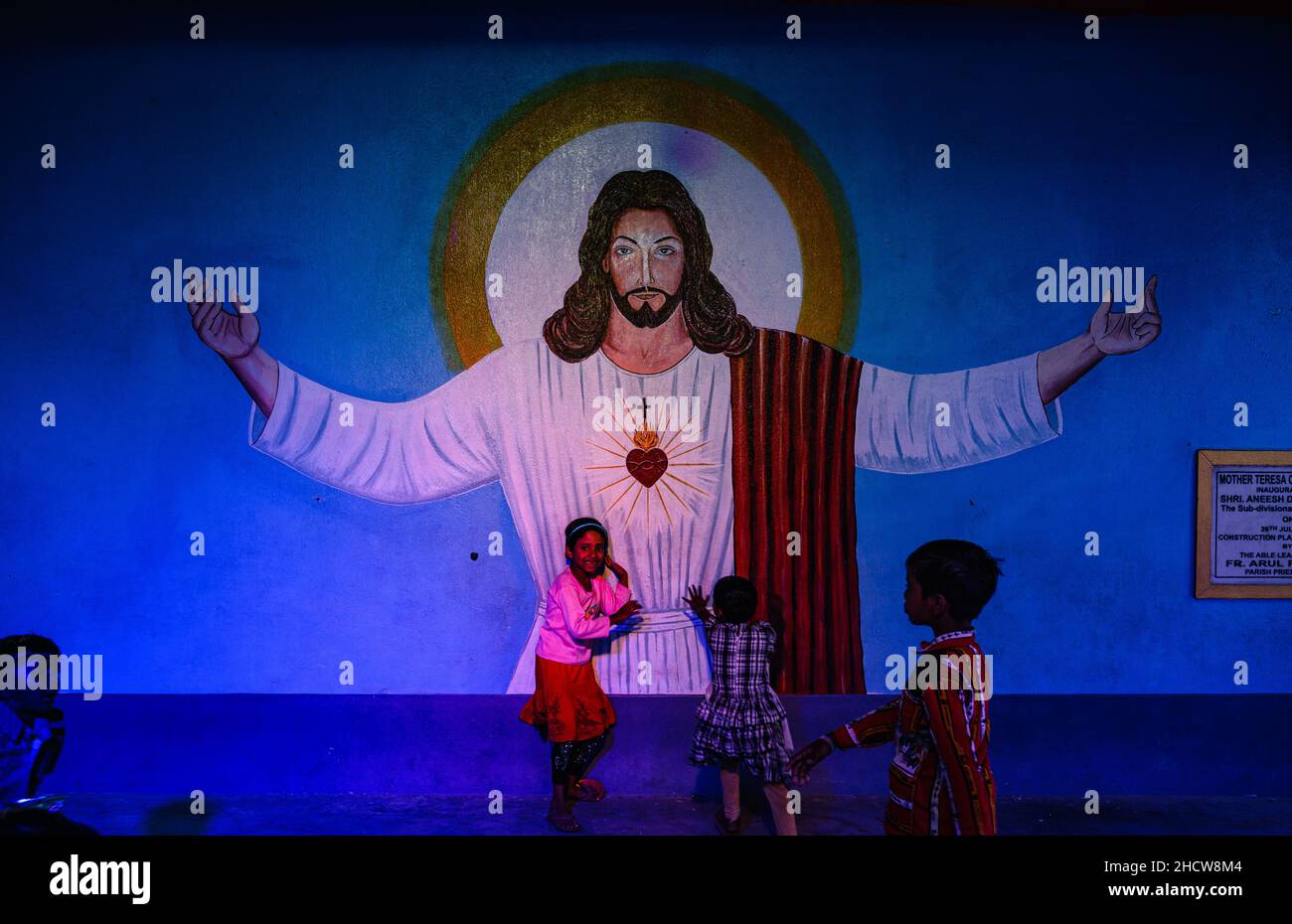 Des enfants de différents villages lointains célèbrent le Saint Noël dans une petite église et jouent devant une grande photo de Jésus-Christ à Haulia, Bengale occidental, Inde. Banque D'Images