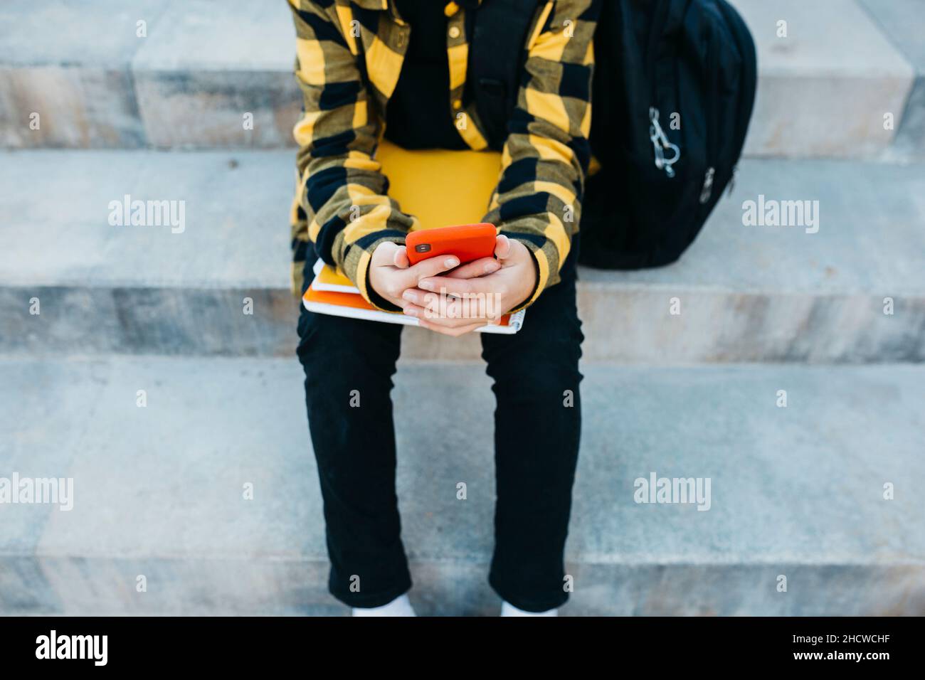 Gros plan des mains de l'adolescent à l'aide d'un smartphone rouge et assis sur les escaliers Banque D'Images