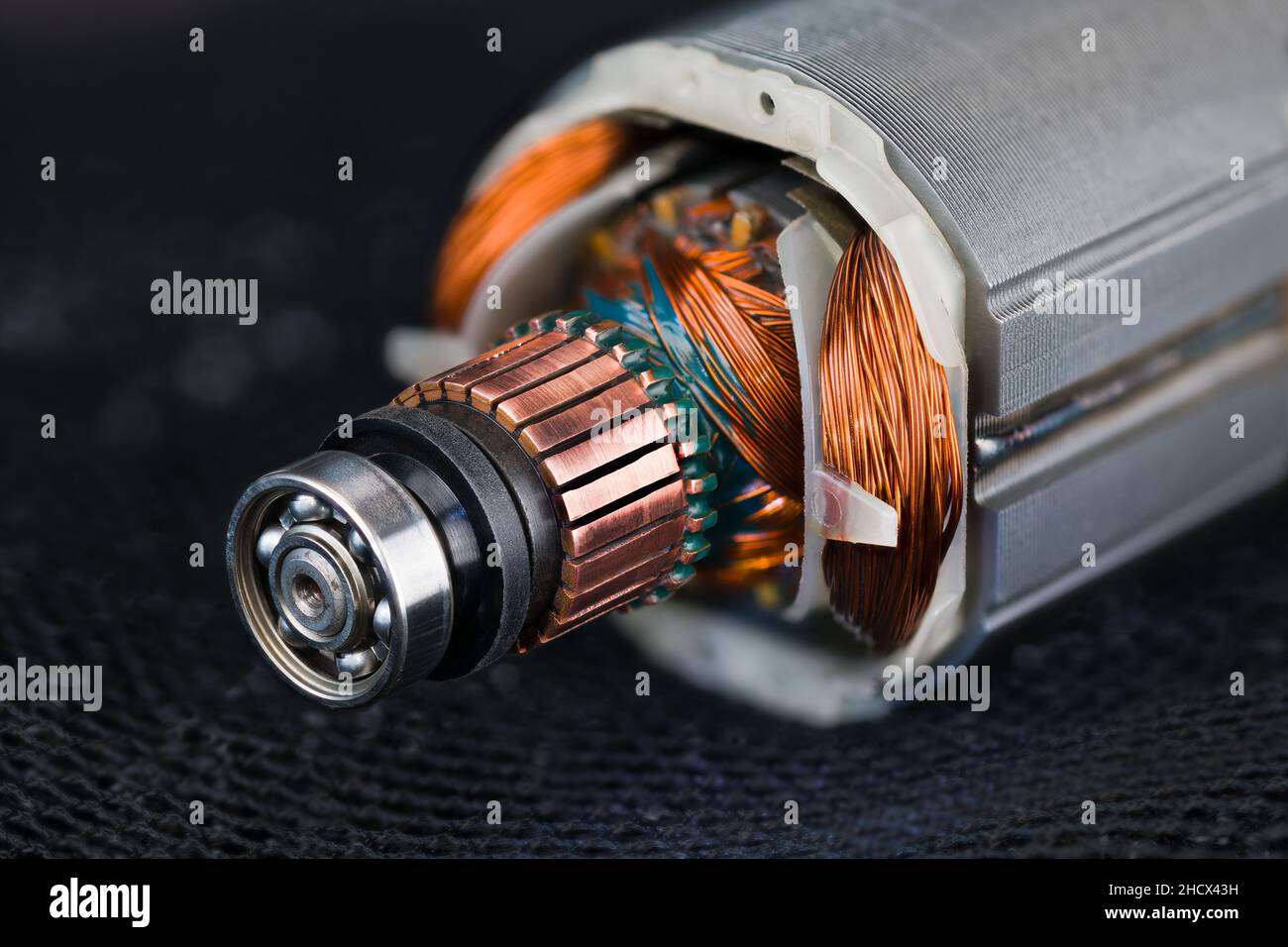 Détail du rotor et du stator du moteur CC électrique sur fond de maille noire.Gros plan du roulement à billes en acier, du collecteur en cuivre ou des fils de bobine sur un filet bleu foncé. Banque D'Images