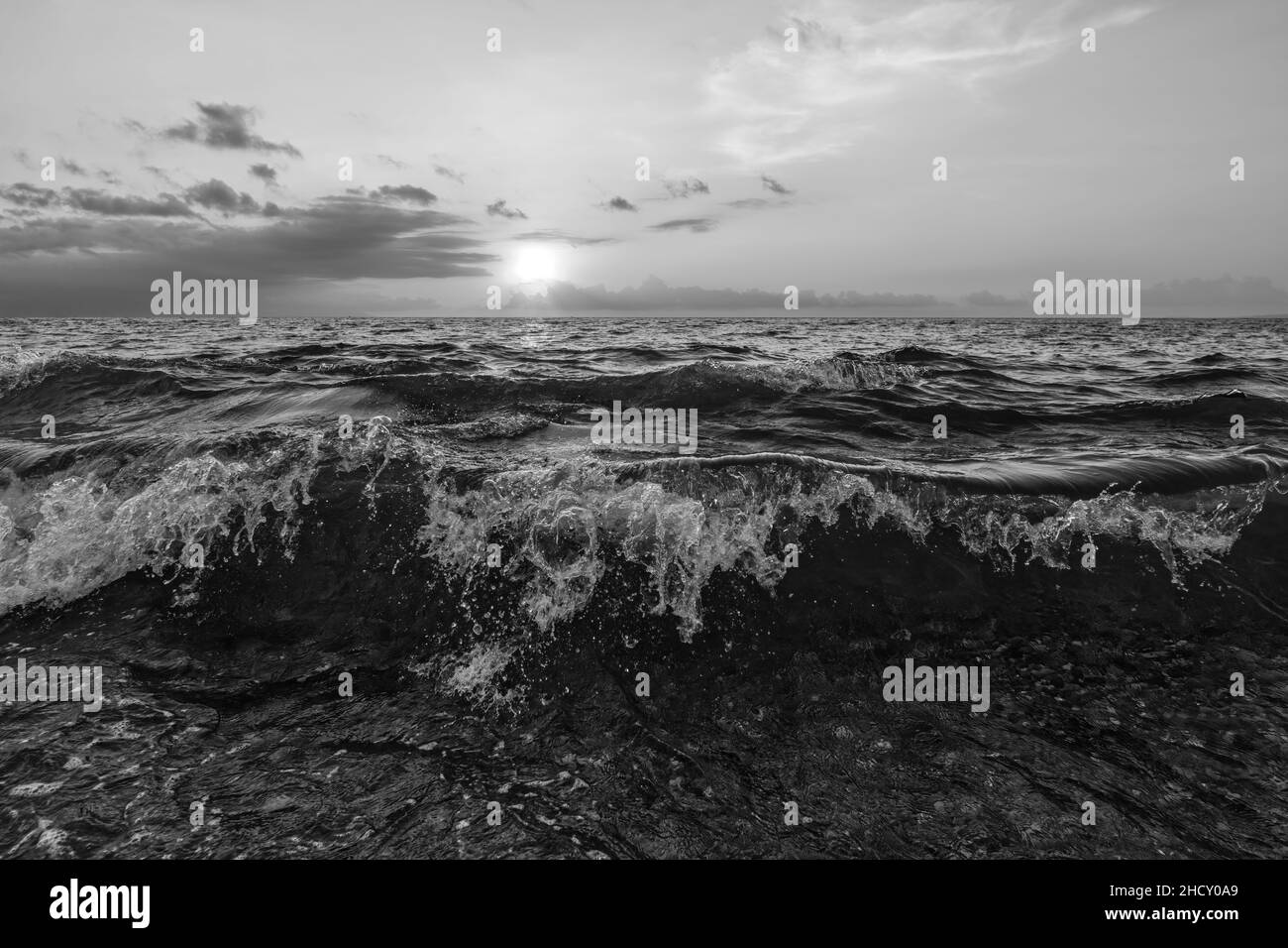 Un ciel de coucher de soleil sur Ocean Seascape avec Un paysage cloudscape détaillé comme Une vague tombe en terre au format d'image noir et blanc Banque D'Images