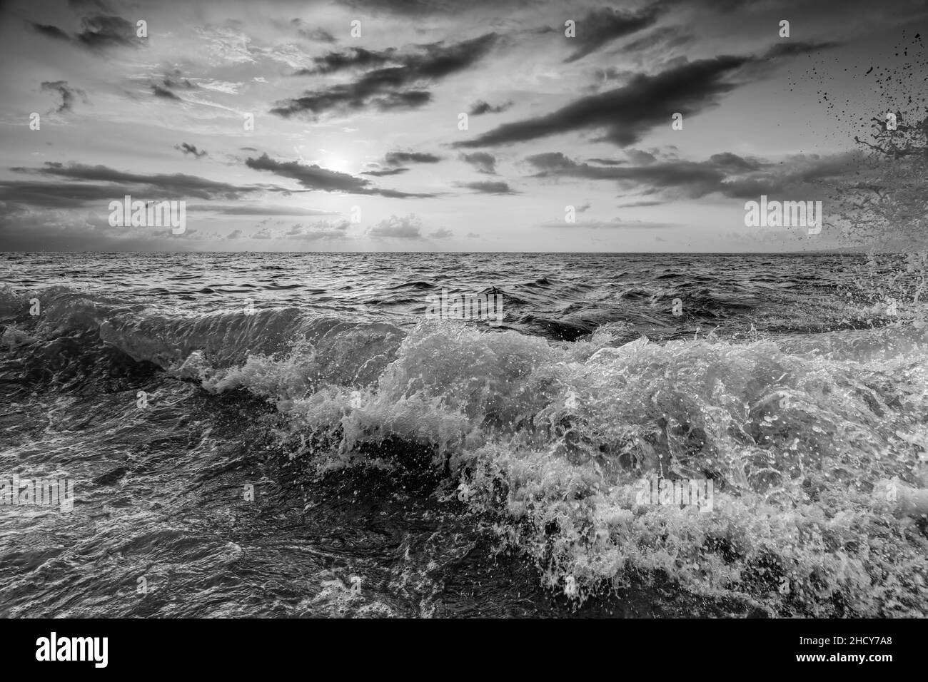 Un ciel de coucher de soleil sur Ocean Seascape avec Un paysage cloudscape détaillé comme Une vague tombe en terre au format d'image noir et blanc Banque D'Images
