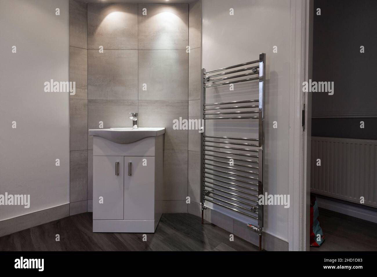 Salle de bains moderne avec meuble-lavabo, grands carreaux blancs Barrington, sol en vinyle LVT, murs gris et blancs, grand porte-serviettes, spots Banque D'Images