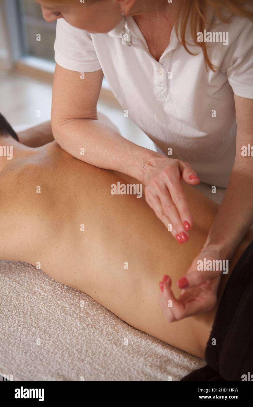 Coupe courte verticale d'un masseur professionnel féminin travaillant au centre de spa, massant le dos d'un client masculin Banque D'Images