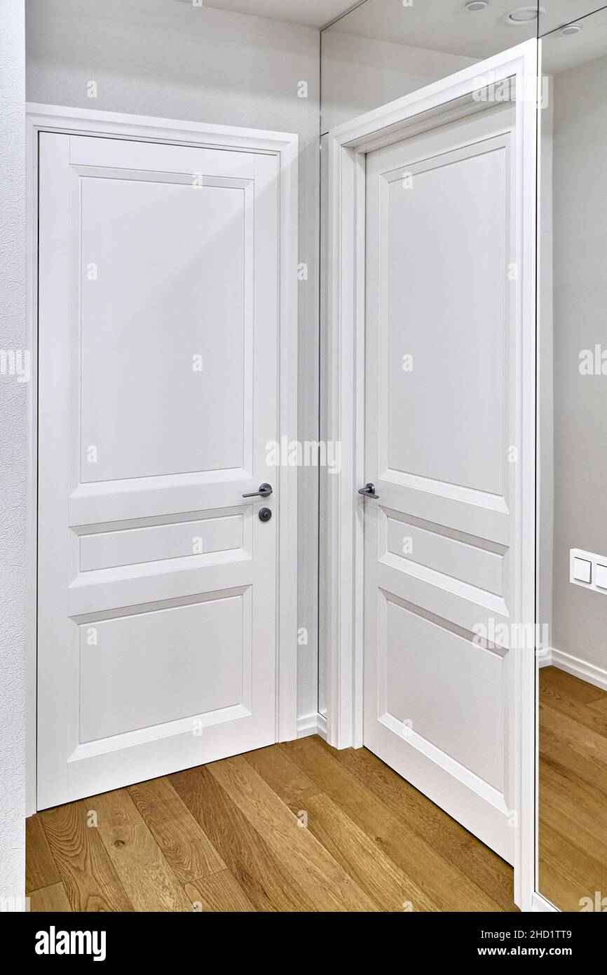 Porte blanche fermée classique et interrupteurs lumineux sur un mur miroir propre dans une chambre spacieuse et décorée dans un appartement de luxe Banque D'Images