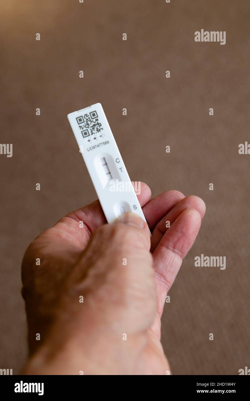 Échantillon de test de débit latéral Covid 19 montrant un résultat positif dans une main sur fond marron clair. Banque D'Images