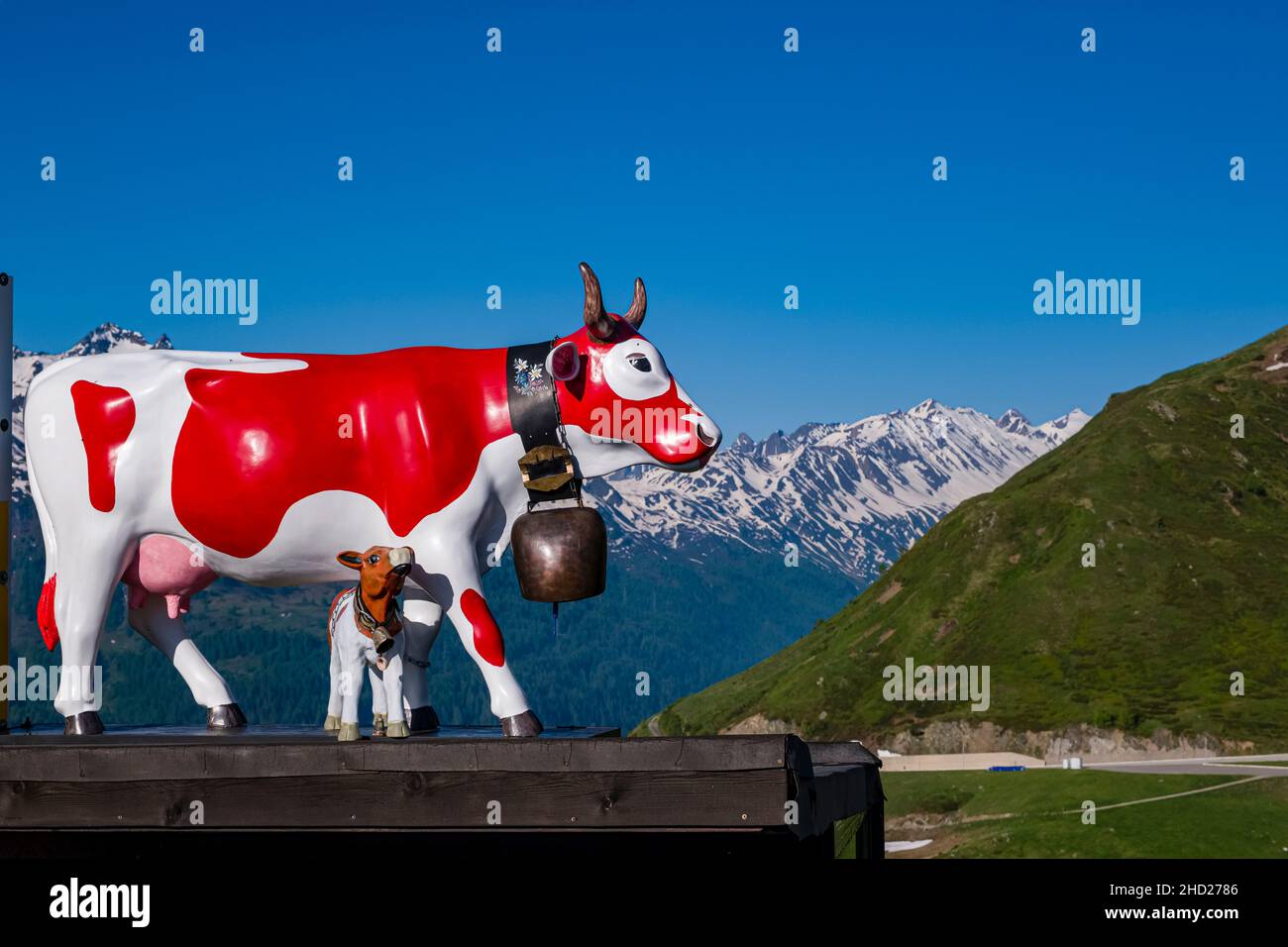 La statue d'une vache et d'un calw peints en rouge et blanc sous le col de Gotthard, des montagnes enneigées au loin. Banque D'Images