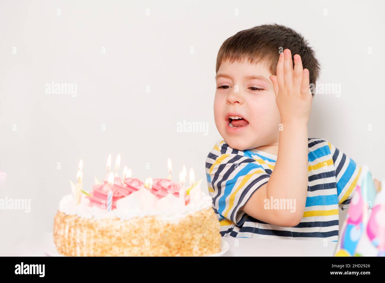 Le garçon est bouleversé, célébrant son anniversaire, pleurant assis à la table avec un gâteau, un endroit pour le texte. Banque D'Images