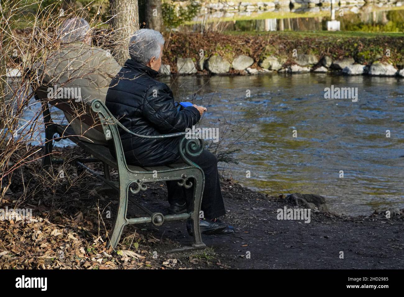 Un couple à la retraite aux cheveux gris est assis sur un banc dans un parc sur la rive d'une petite rivière. Banque D'Images