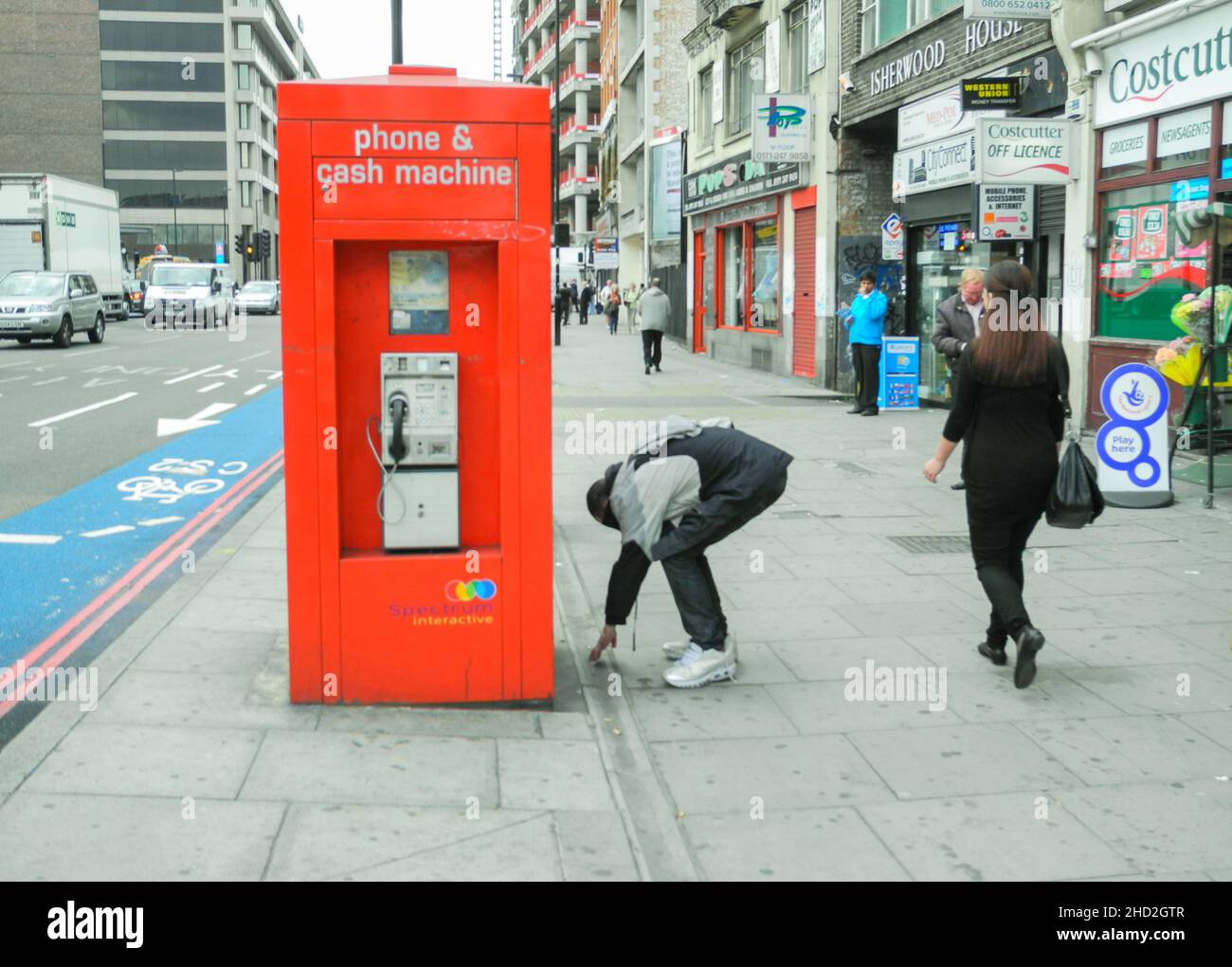 Un homme s'attèle à prendre une cigarette, mais sur Whitechapel High Street, Whitechapel, Londres, Angleterre, Royaume-Uni Banque D'Images