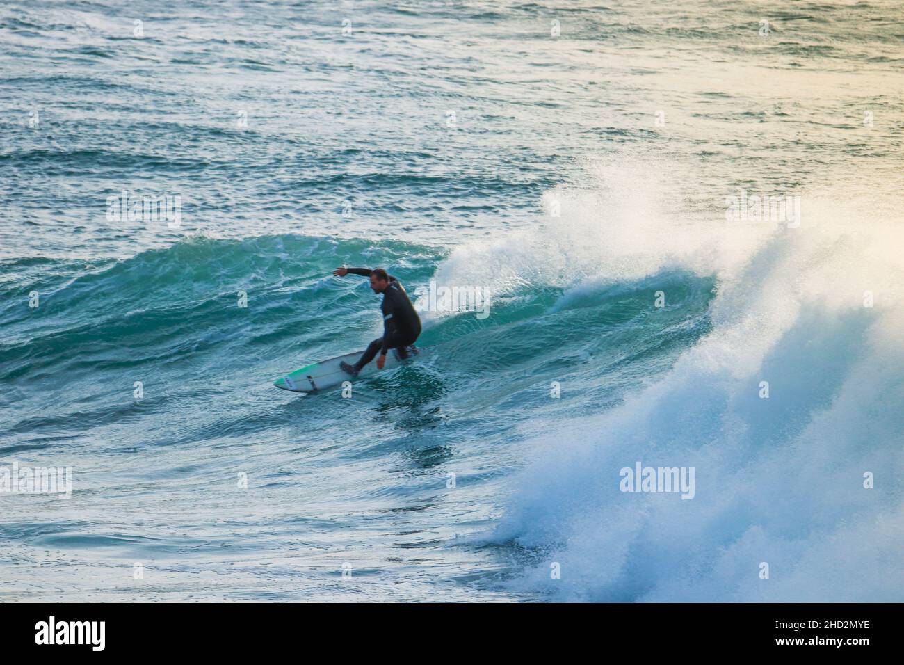 Surfer sur une vague bleue à un jour ensoleillé à Ericeira au Portugal. Banque D'Images