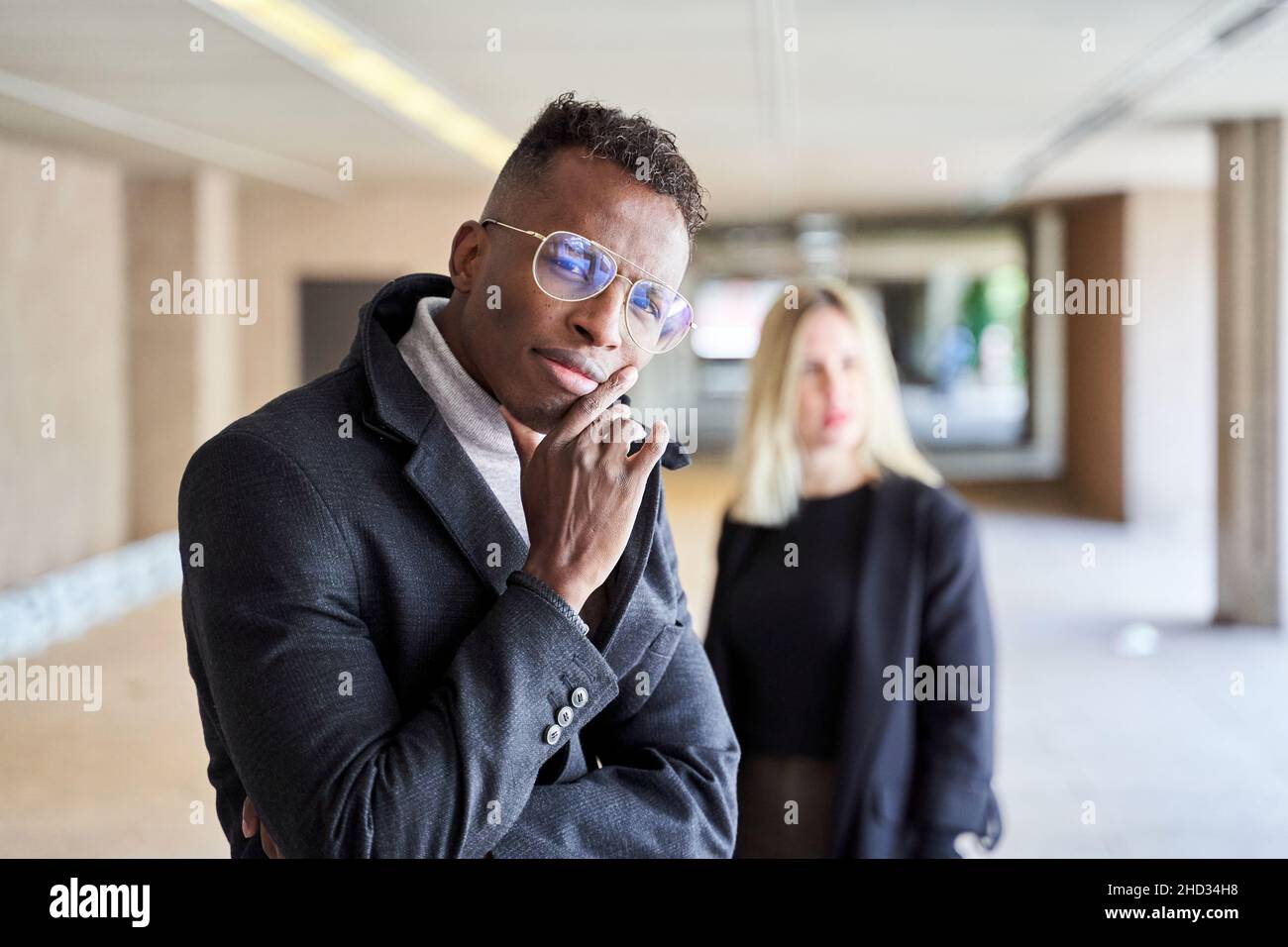 Homme afro-américain en manteau élégant et lunettes regardant l'appareil photo tout en se tenant dans le passage moderne près de la petite amie Banque D'Images