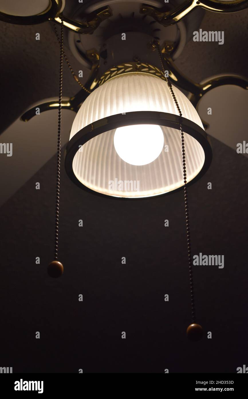 Gros plan à angle bas d'un ventilateur de plafond avec la lumière allumée et les fils suspendus dans une chambre d'hôtel Banque D'Images