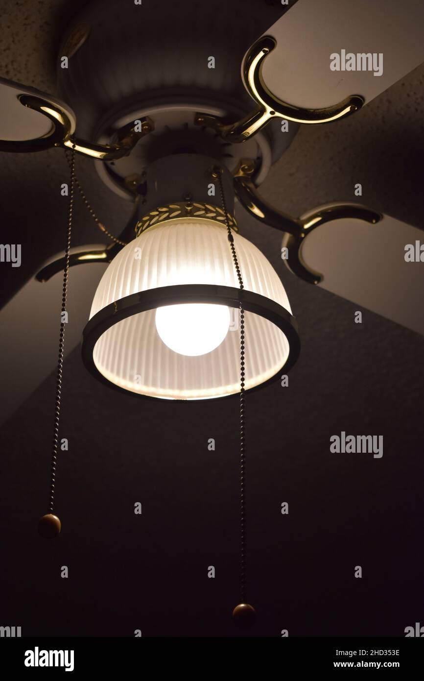 Gros plan à angle bas d'un ventilateur de plafond avec la lumière allumée et les fils suspendus dans une chambre d'hôtel Banque D'Images