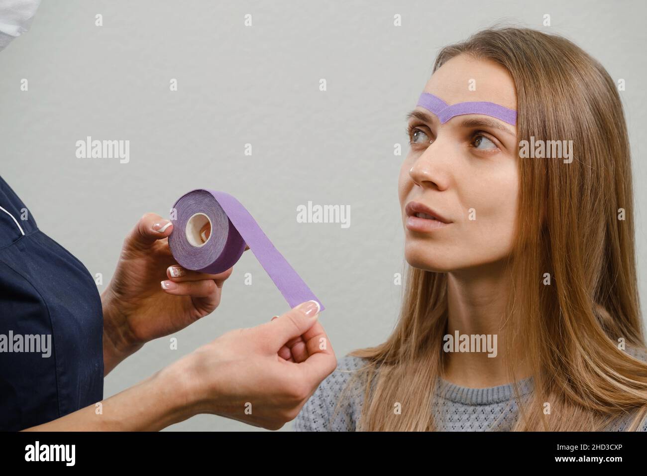 une esthéticienne féminine qui fait le maquillage kinésio du visage.Rayures violettes sur le front contre les rides et le vieillissement.Médecine alternative pour Banque D'Images une esthéticienne féminine qui fait le maquillage kinésio du visage.Rayures violettes sur le front contre les rides et le vieillissement.Médecine alternative pour Banque D'Images