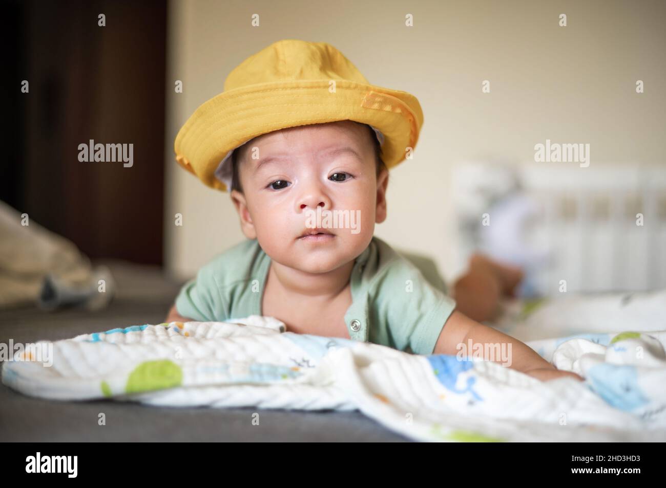 Adorable garçon de 2 mois de course mixte nouveau-né portant un chapeau et allongé sur son ventre sur la tête de levage du lit et jouant entouré de jouets Banque D'Images