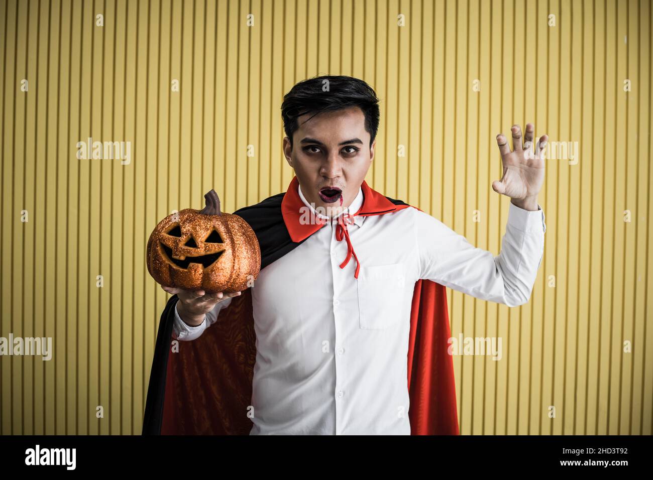 Halloween concept de jeune asiatique en costume dracula et tenir Halloween citrouille orange sur fond jaune.Portrait de l'adolescent habillé comme la dra Banque D'Images