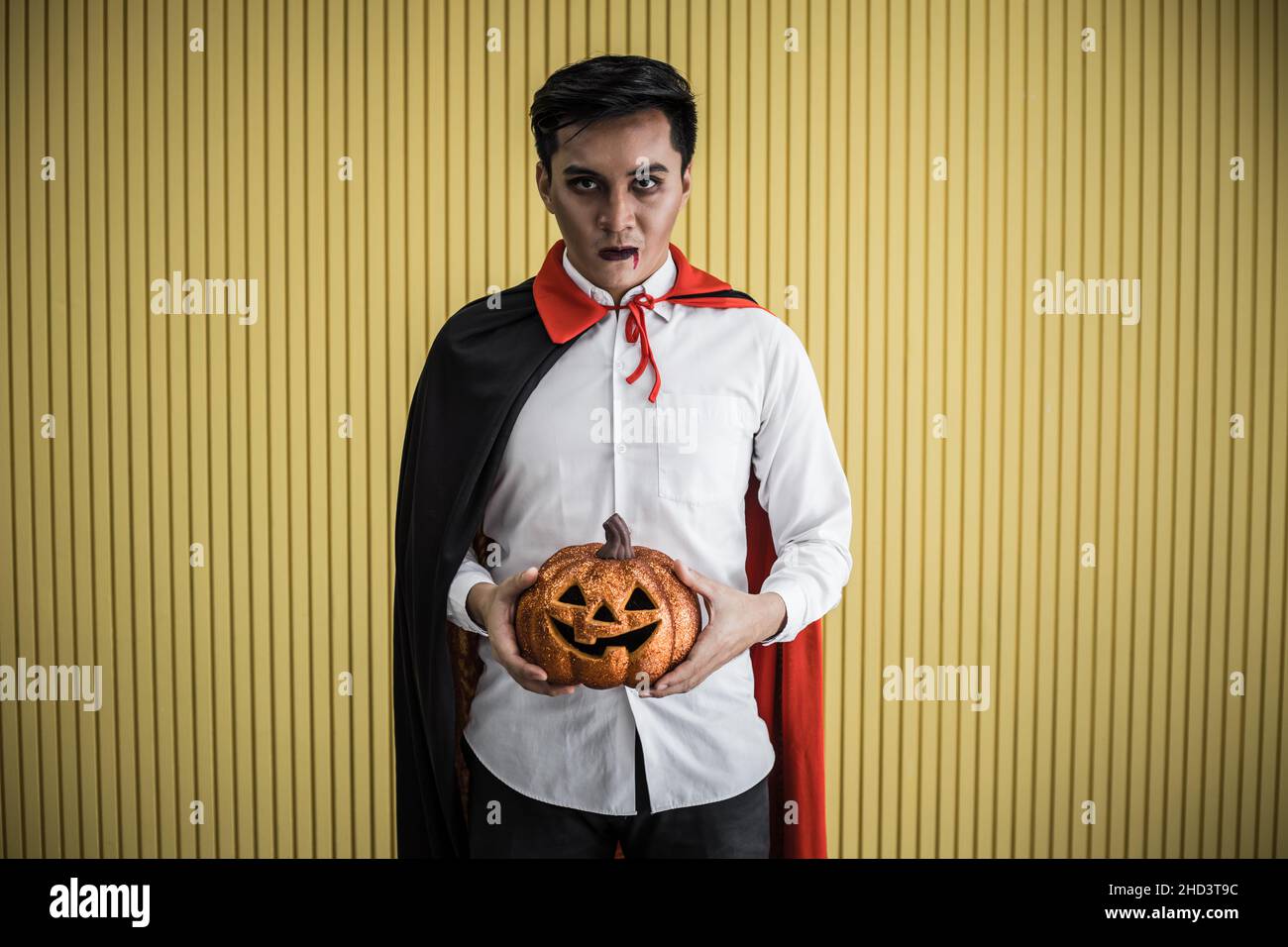 Halloween concept de jeune asiatique en costume dracula et tenir Halloween citrouille orange sur fond jaune.Portrait de l'adolescent habillé comme la dra Banque D'Images