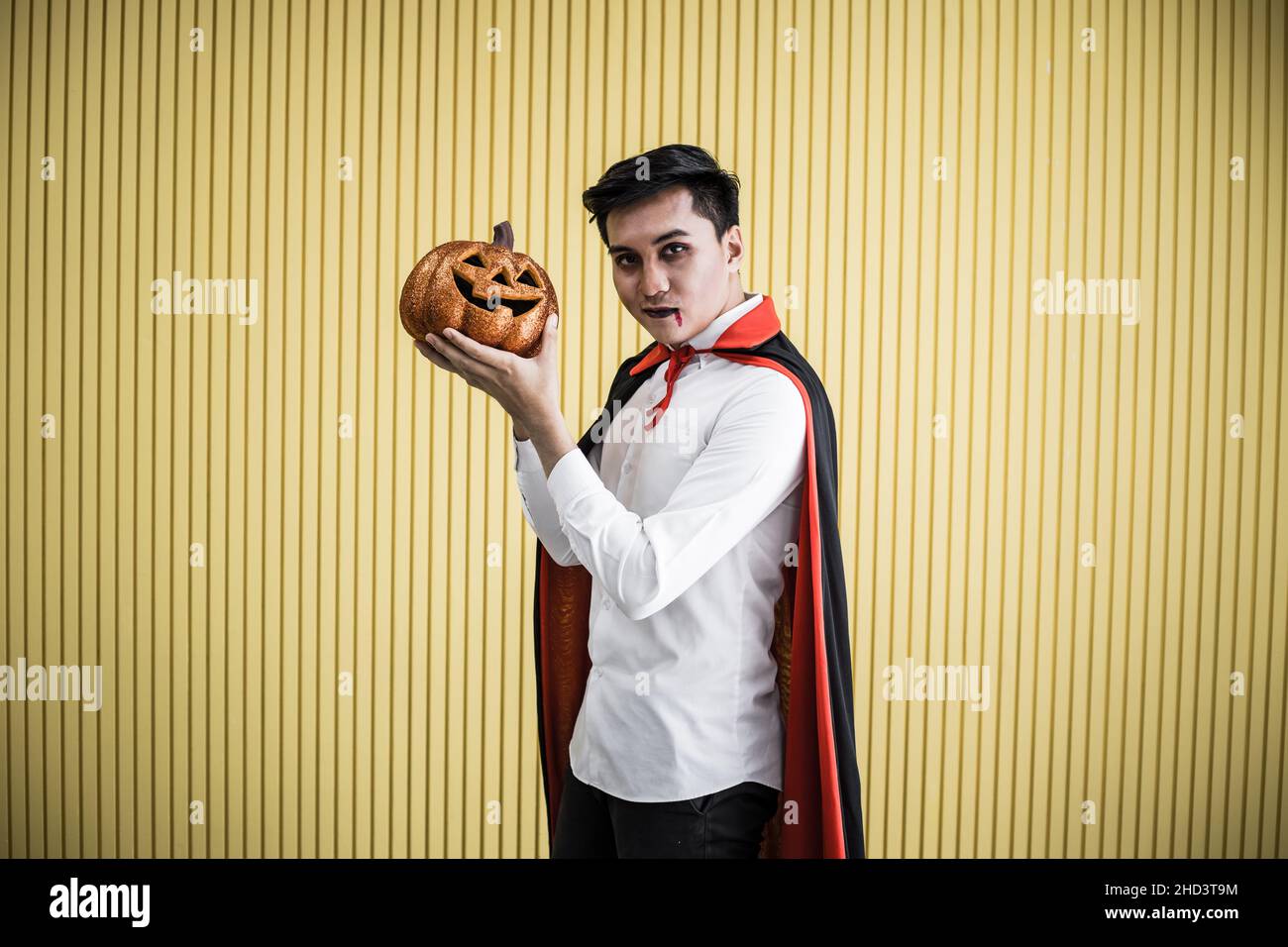 Halloween concept de jeune asiatique en costume dracula et tenir Halloween citrouille orange sur fond jaune.Portrait de l'adolescent habillé comme la dra Banque D'Images