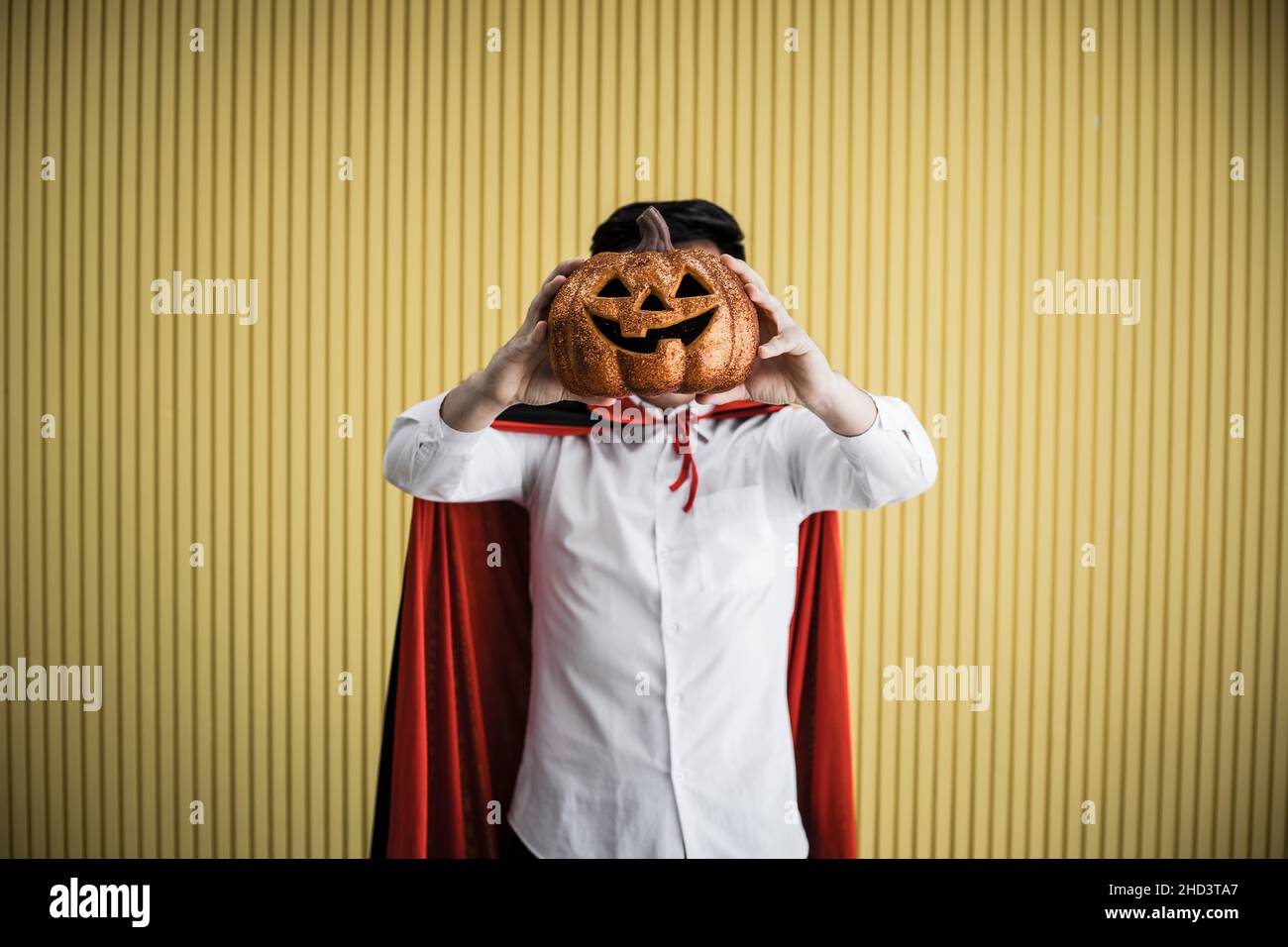 Halloween concept de jeune asiatique en costume dracula et tenir Halloween citrouille orange sur fond jaune.Portrait de l'adolescent habillé comme la dra Banque D'Images