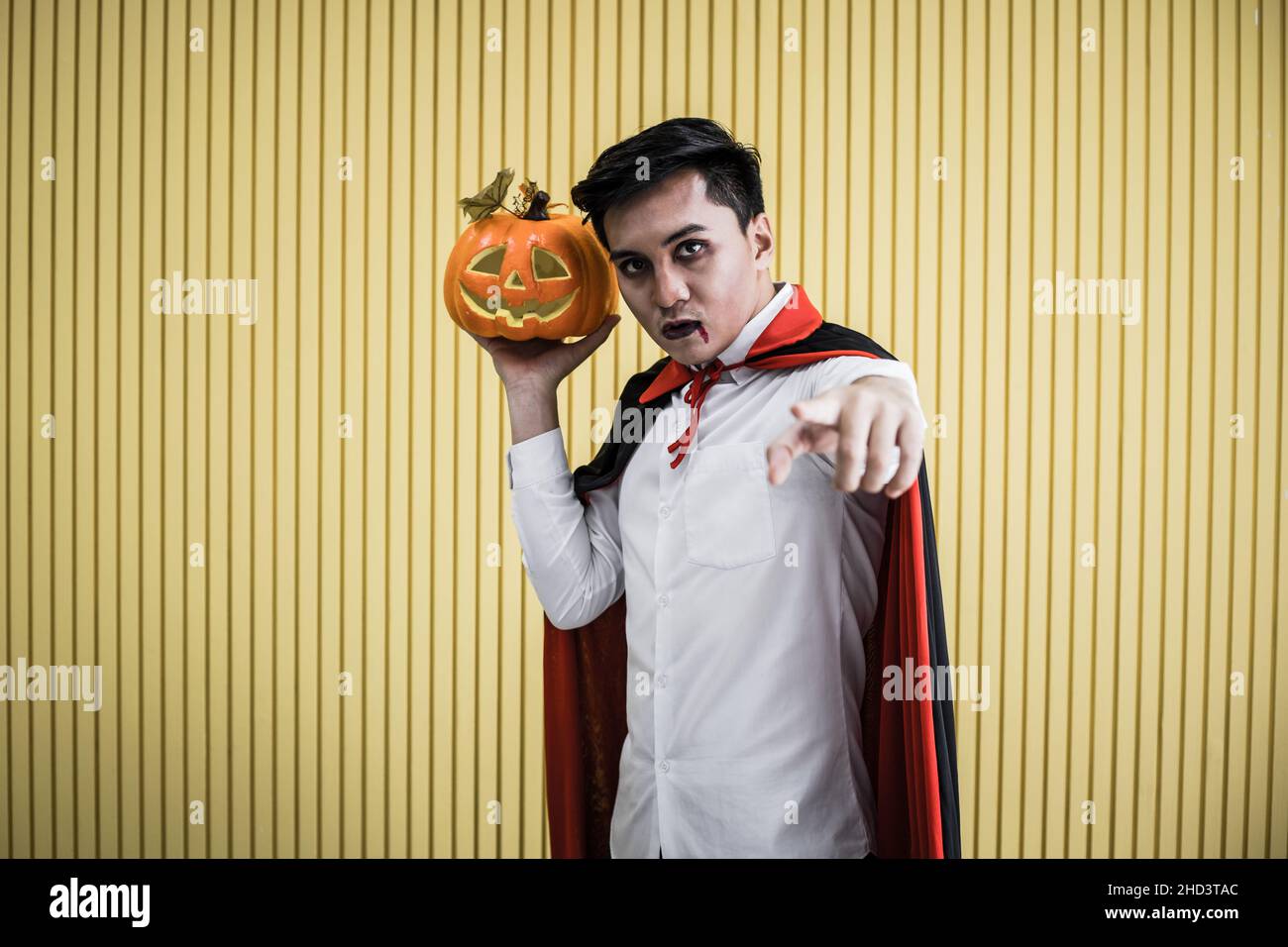 Halloween concept de jeune asiatique en costume dracula et tenir Halloween citrouille orange sur fond jaune.Portrait de l'adolescent habillé comme la dra Banque D'Images
