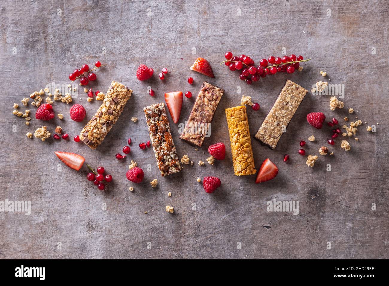 Diverses barres de muesli avec des raisins de Corinthe, des framboises et des fraises, ainsi que des céréales autour d'elles, vue du dessus. Banque D'Images