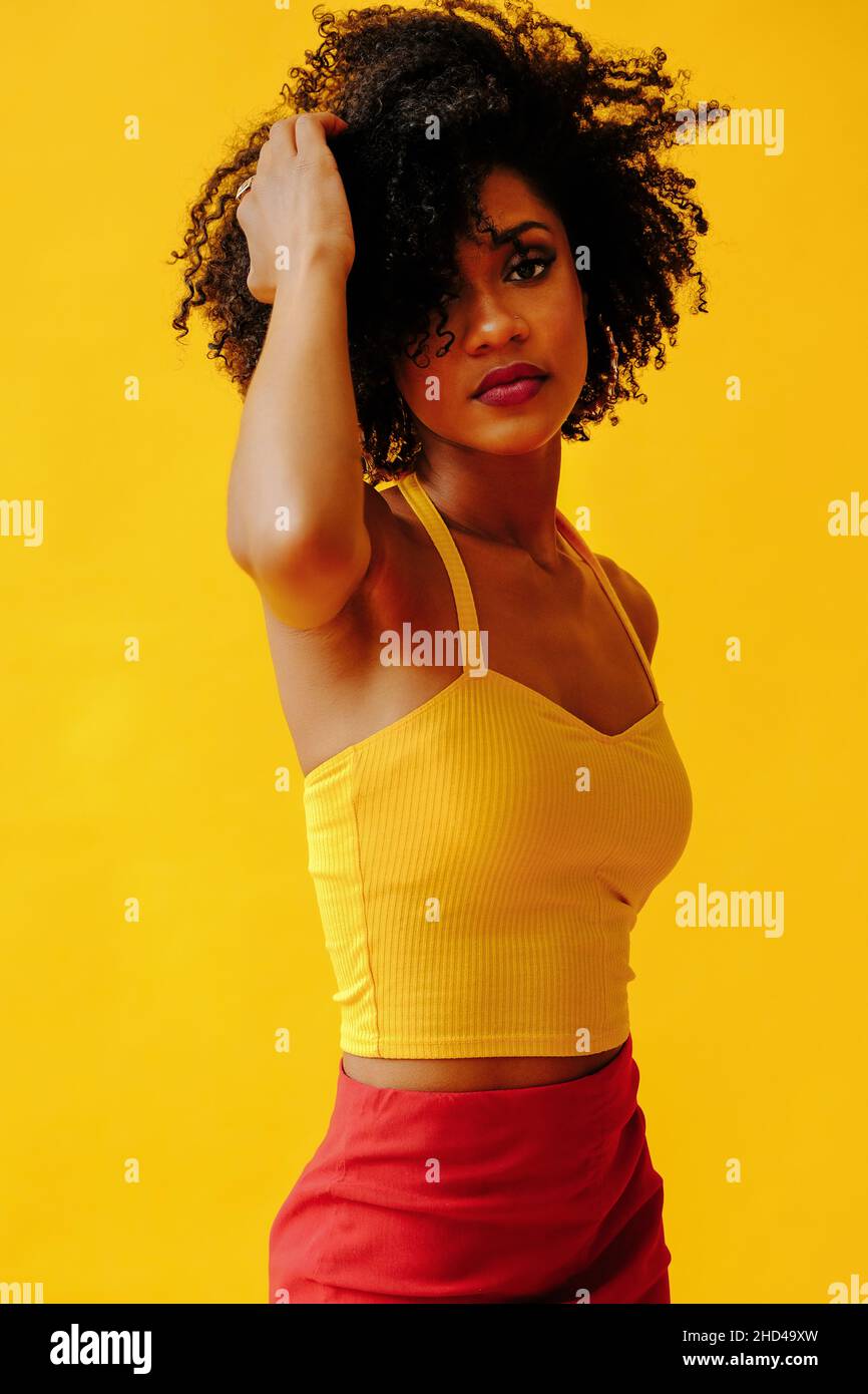 Belle jeune femme afro-américaine en tenue d'été lumineuse posant isolée sur fond jaune Banque D'Images