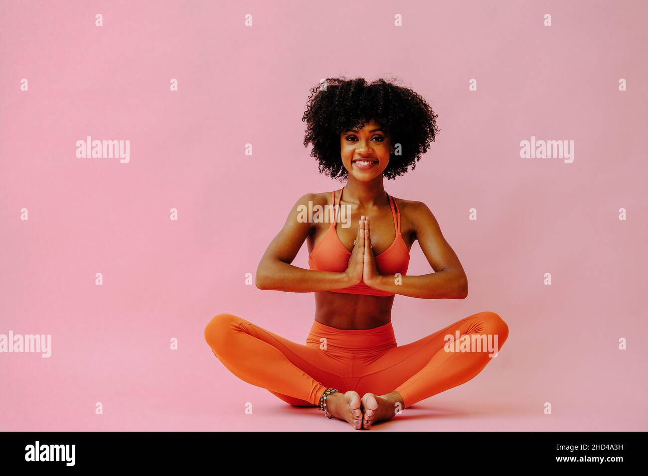 Belle femme afro-américaine méditant dans les tenues de sport sur fond rose Banque D'Images
