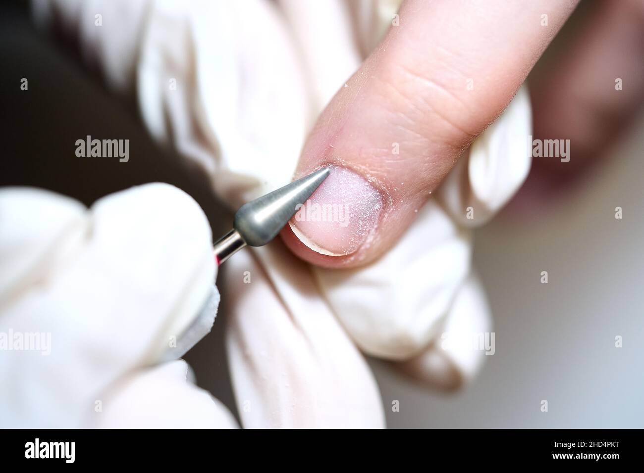 Femme en salon de manucure au salon de beauté par esthéticienne qui utilise le foret électrique pour lime à ongles avec la poussière et les débris volants éclatés autour.Concept de soin des ongles. Banque D'Images