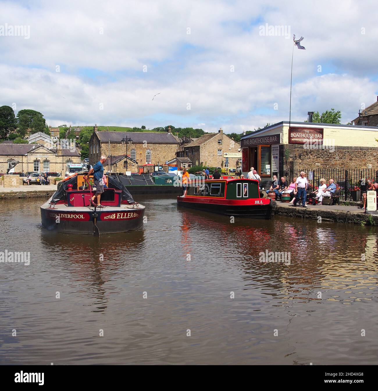 Les touristes regardent une barge de cargaison qui passe et profitent du soleil au bassin du canal de Skipton dans le Yorkshire, en Angleterre. Banque D'Images