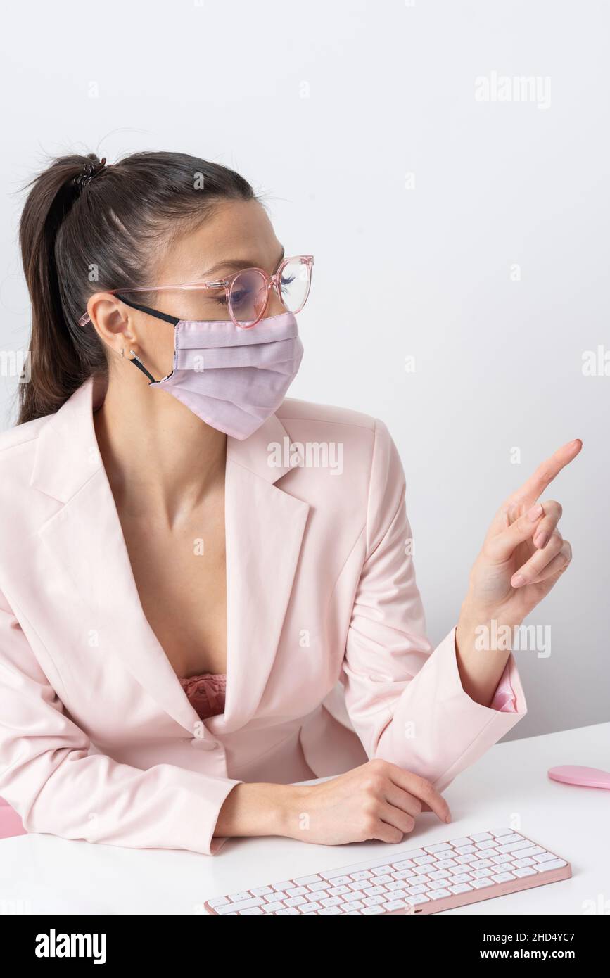 Salisbury, Wiltshire, Royaume-Uni.2021. Femme attrayante portant le masque rose et pointant vers l'ordinateur et le clavier. Banque D'Images