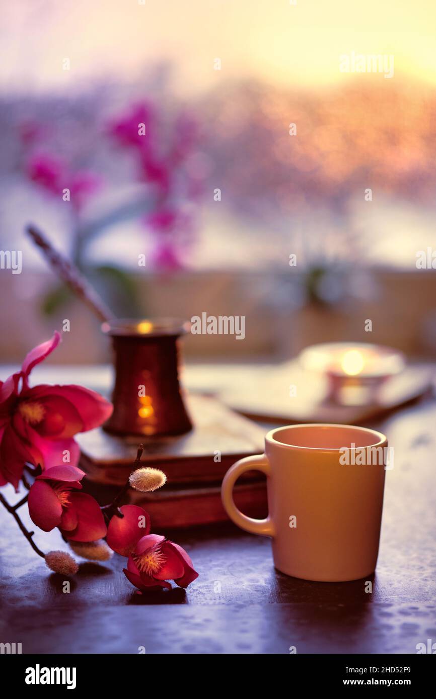 Café oriental cuisiné dans une cafetière traditionnelle turque en cuivre sur des livres anciens.Tasse en céramique au premier plan.L'hiver avec les vieux livres.Fenêtre de coucher de soleil Banque D'Images