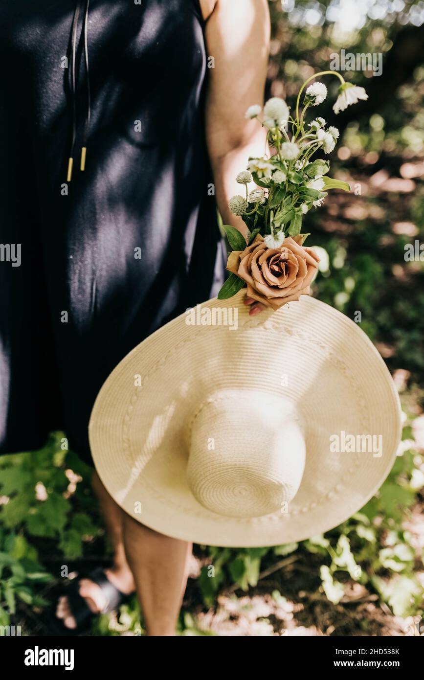 Gros plan d'une femme tenant des fleurs fraîchement cueillies et un grand chapeau de soleil Banque D'Images