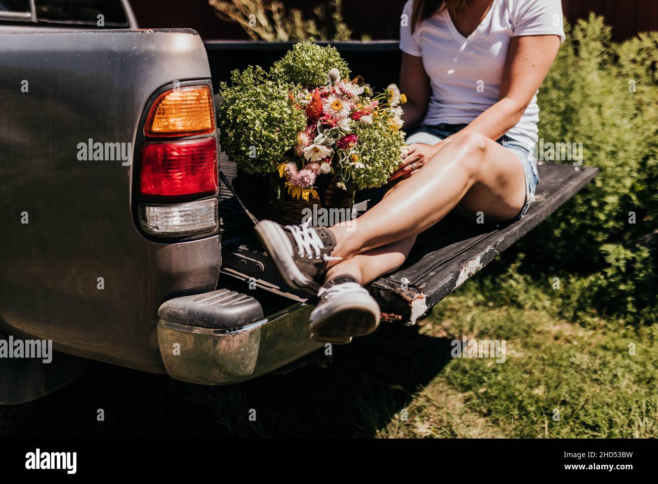 La femme est assise sur la porte de queue du camion avec une caisse de fleurs pendant l'été Banque D'Images