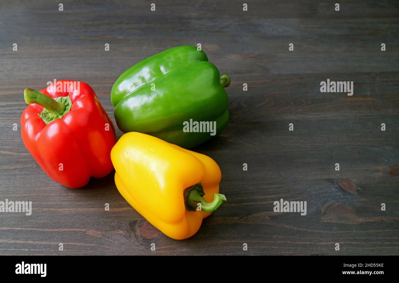 Peppers tricolores vibrants alignés sur un arrière-plan en bois Banque D'Images