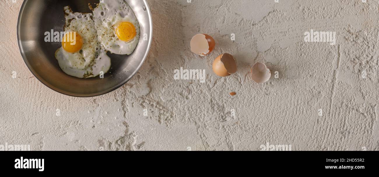 Deux œufs frits dans une casserole de cuivre et des coquilles d'œufs sur fond d'argile rugueux et texturé.Concept de petit déjeuner sain. Banque D'Images