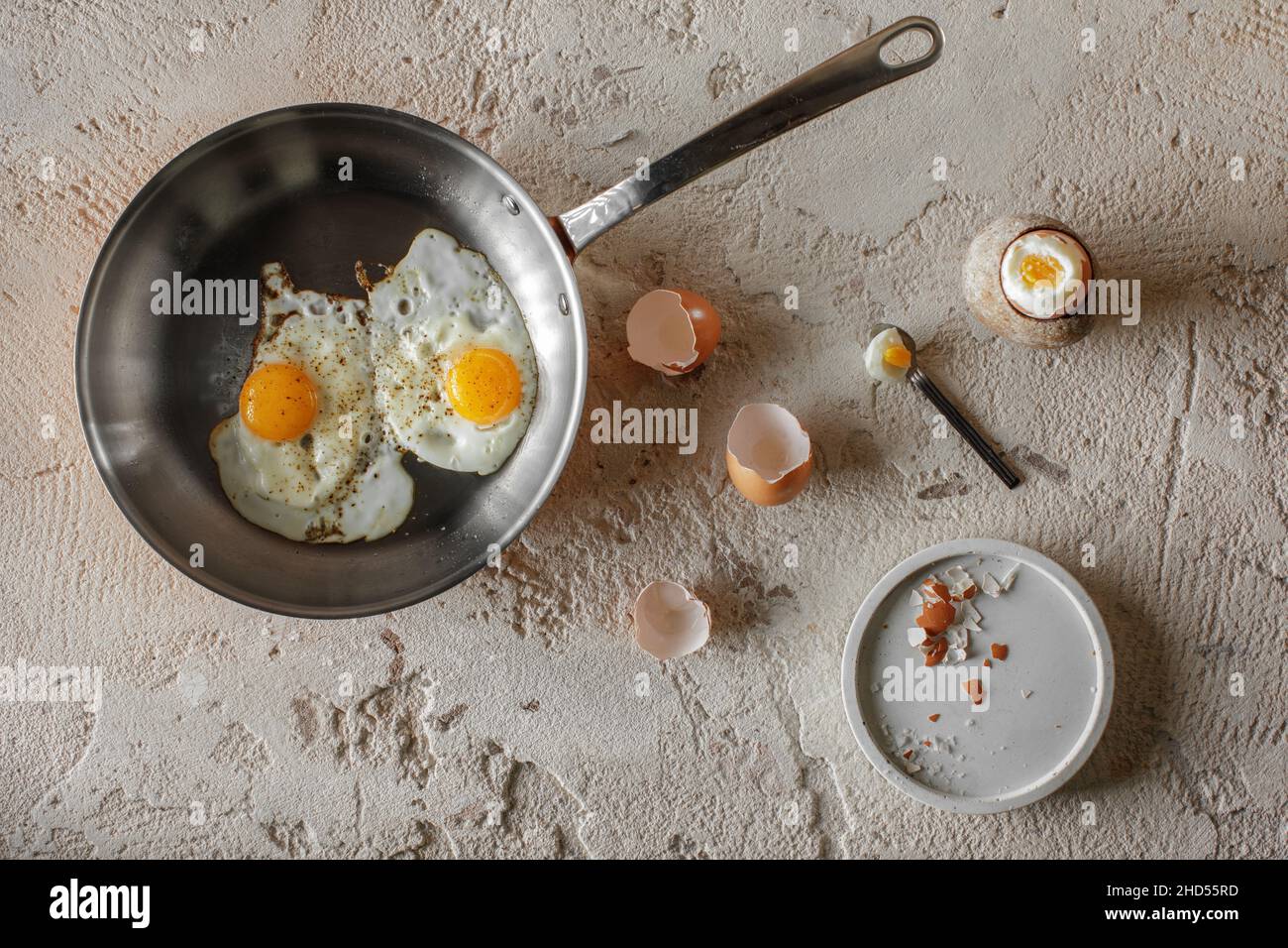 Faites frire deux œufs dans une poêle en cuivre et un œuf dur dans une tasse en grès sur fond d'argile rugueux et texturée.Concept de petit déjeuner sain. Banque D'Images