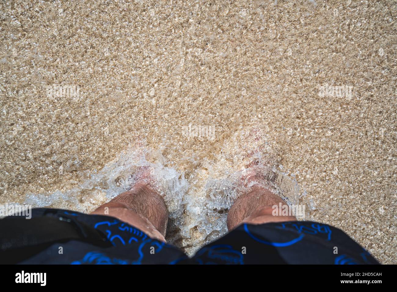 Vue de haut en bas des jambes debout dans une vague arrivant sur une plage blanche Banque D'Images