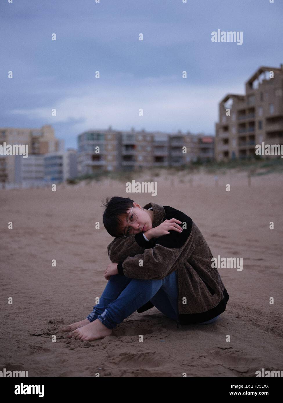 jeune femme non binaire seule sur la plage assise sur le sable Banque D'Images