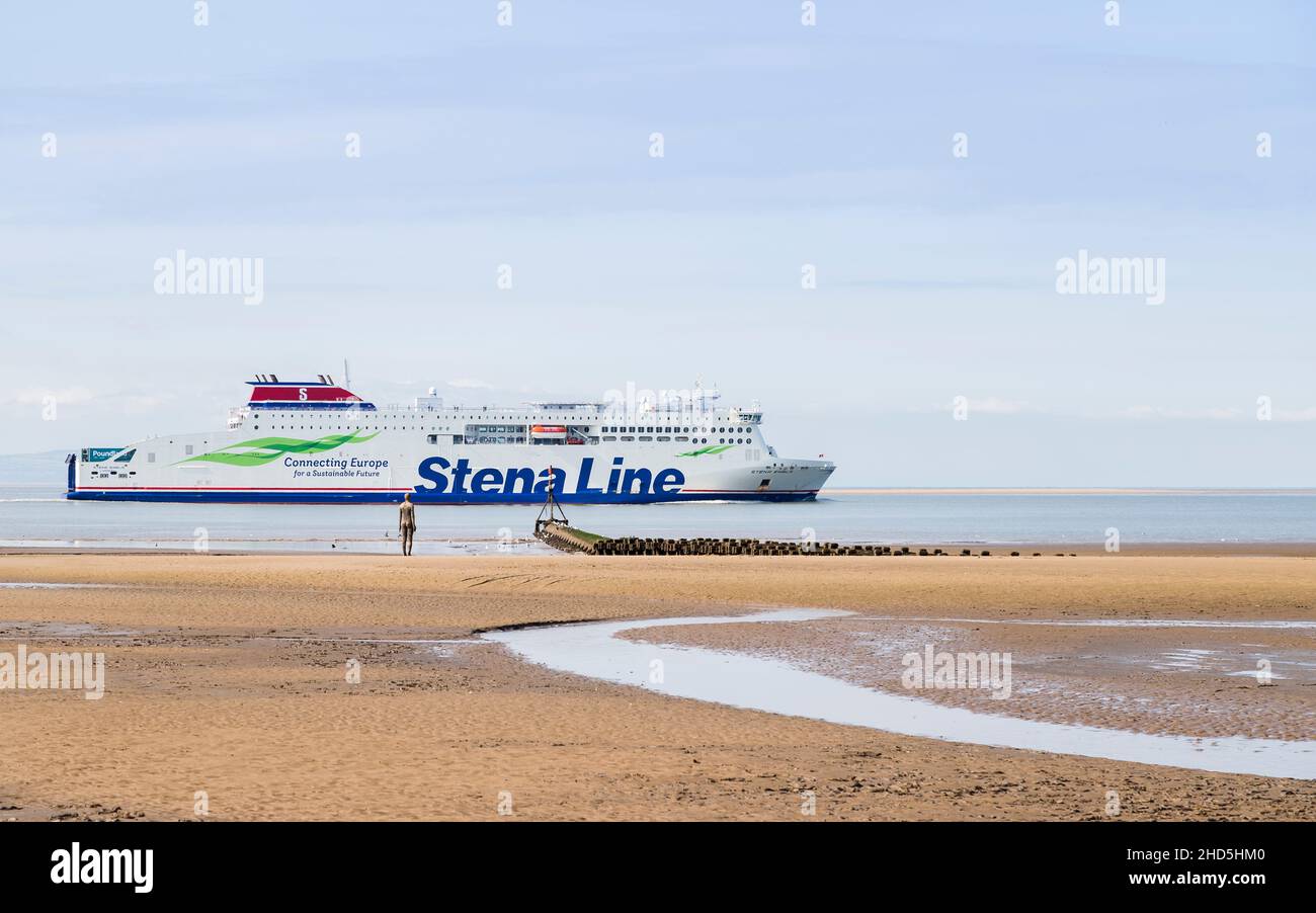 Le ferry Stena Embla quitte la rivière Mersey en passant par un Iron Man sur la plage de Crosby. Banque D'Images