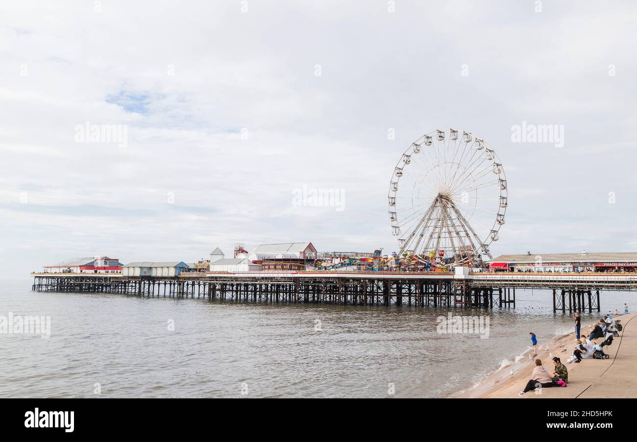 Les touristes s'assoient sur les marches du front de mer de Blackpool en regardant la roue de ferris tourner sur Central Pier. Banque D'Images
