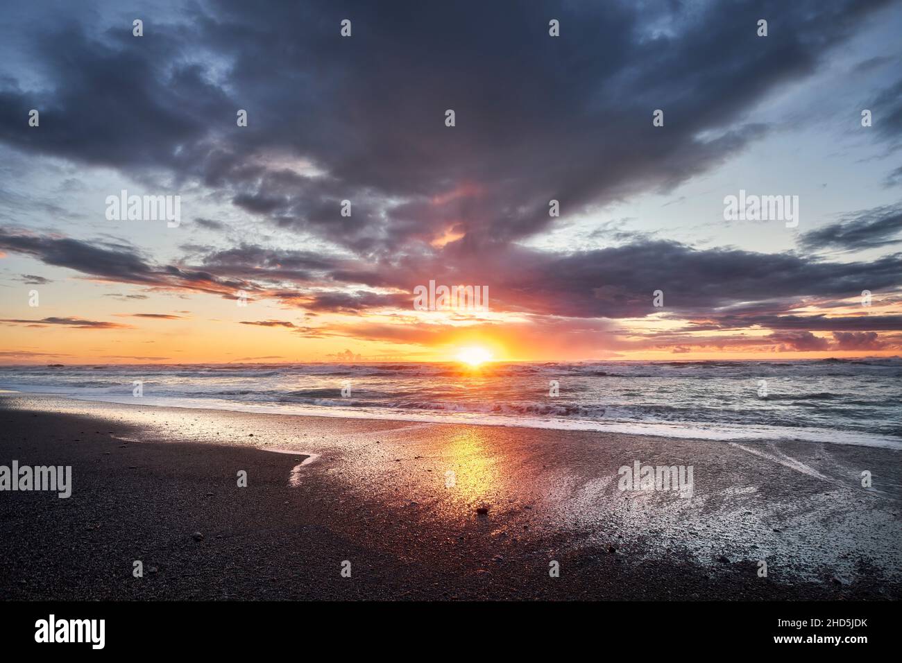 Coucher de soleil sur une plage noire déserte avec des vagues qui se lanceraient sur le rivage. Banque D'Images