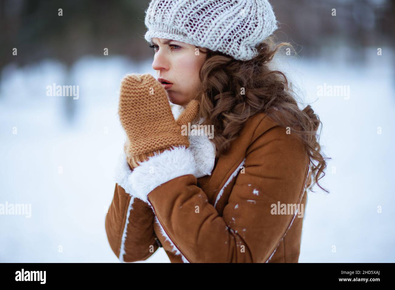 femme moderne de 40 ans avec moufles dans un bonnet tricoté et un manteau  de peau de mouton toussant à l'extérieur dans le parc de la ville en hiver  Photo Stock -