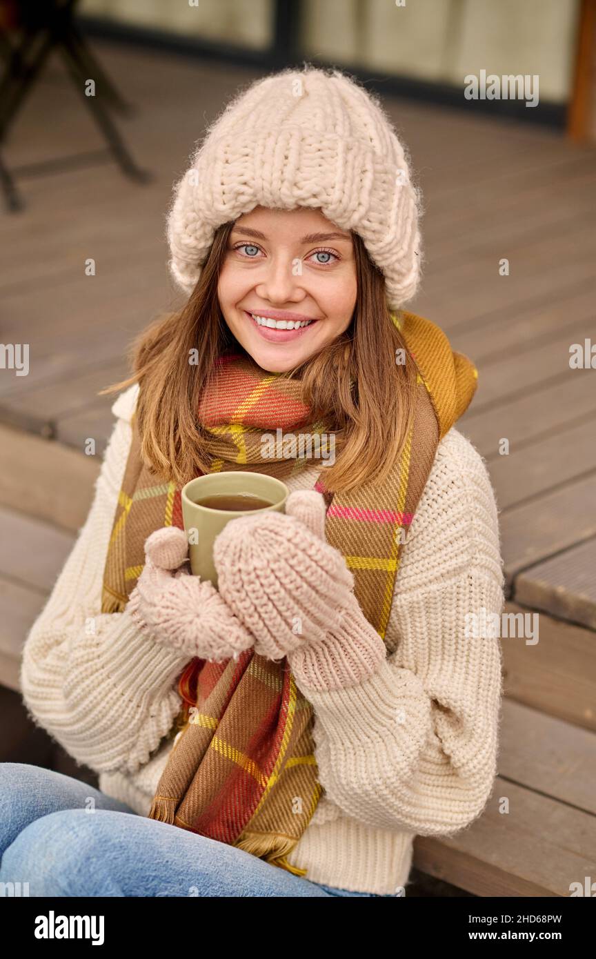 Femme avec café assis sur la véranda regardant l'appareil photo Banque D'Images
