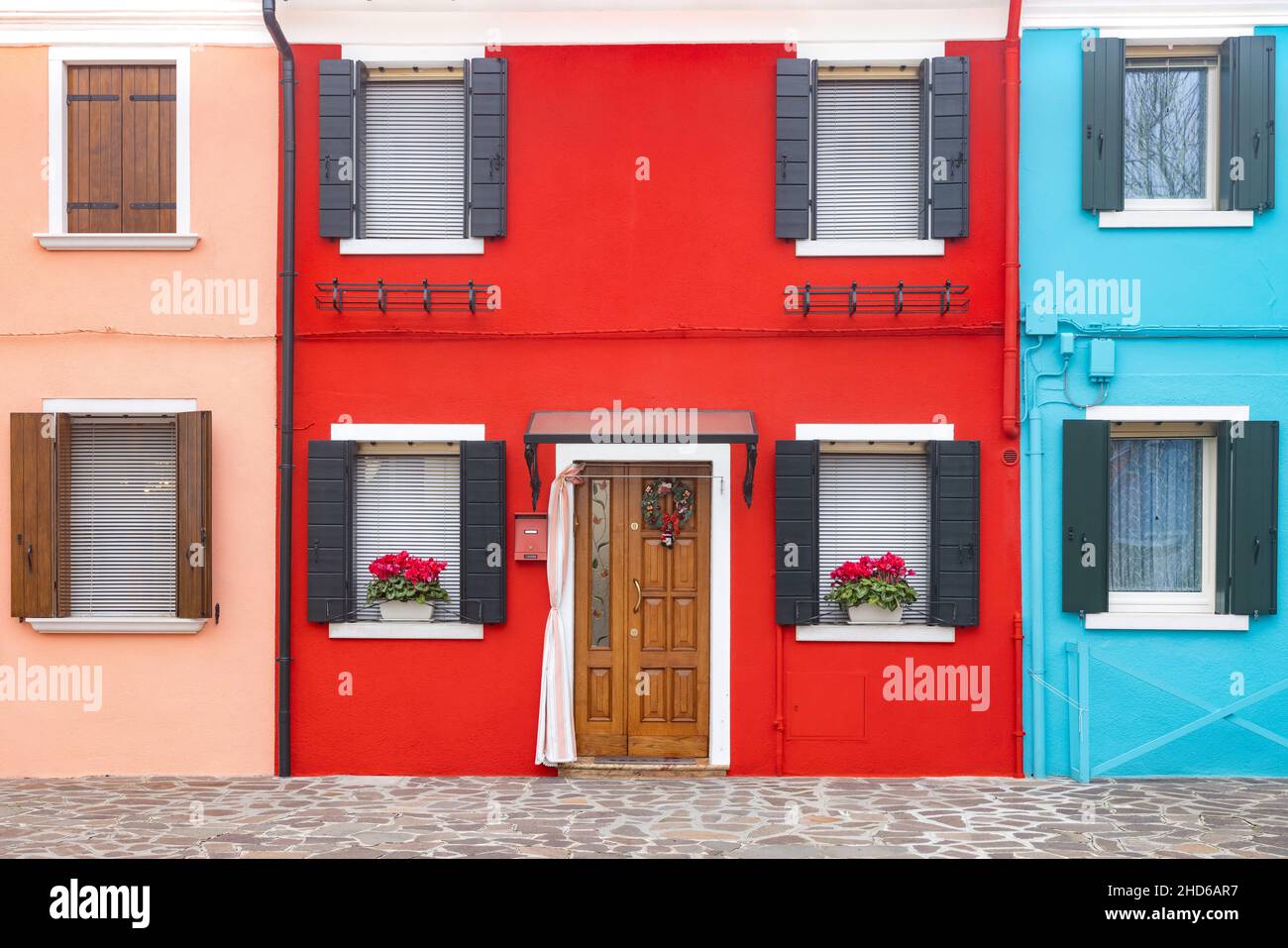 Gros plan d'une façade en plâtre de deux étages aux couleurs vives avec fenêtres avec pots de fleurs et une porte, le plus à gauche rose, centre rouge, le plus à droite bleu Banque D'Images