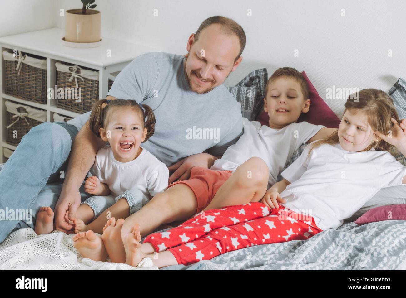 Le père joue avec trois enfants au lit.Papa tille les pieds des enfants.Famille de papa, deux filles et garçon Banque D'Images