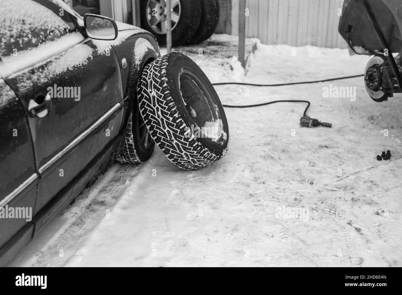 voiture soulevée avec un cric pour le remplacement urgent des roues extérieures, scène hivernale en noir et blanc Banque D'Images