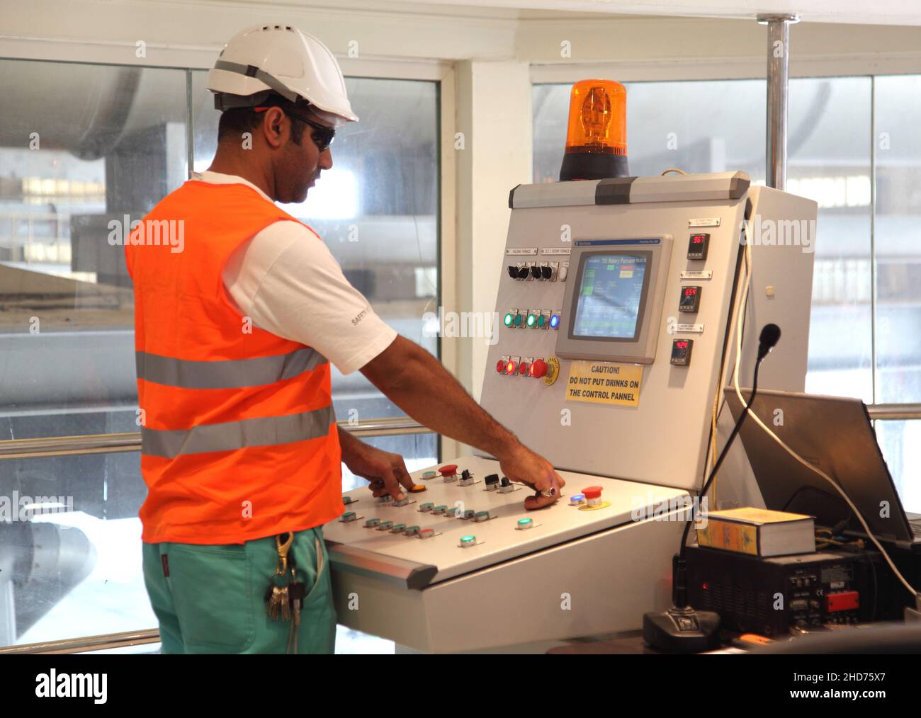 Un ingénieur portant un casque de haute viz et un casque de sécurité fait fonctionner un panneau de commande dans une usine de fusion d'aluminium. Banque D'Images