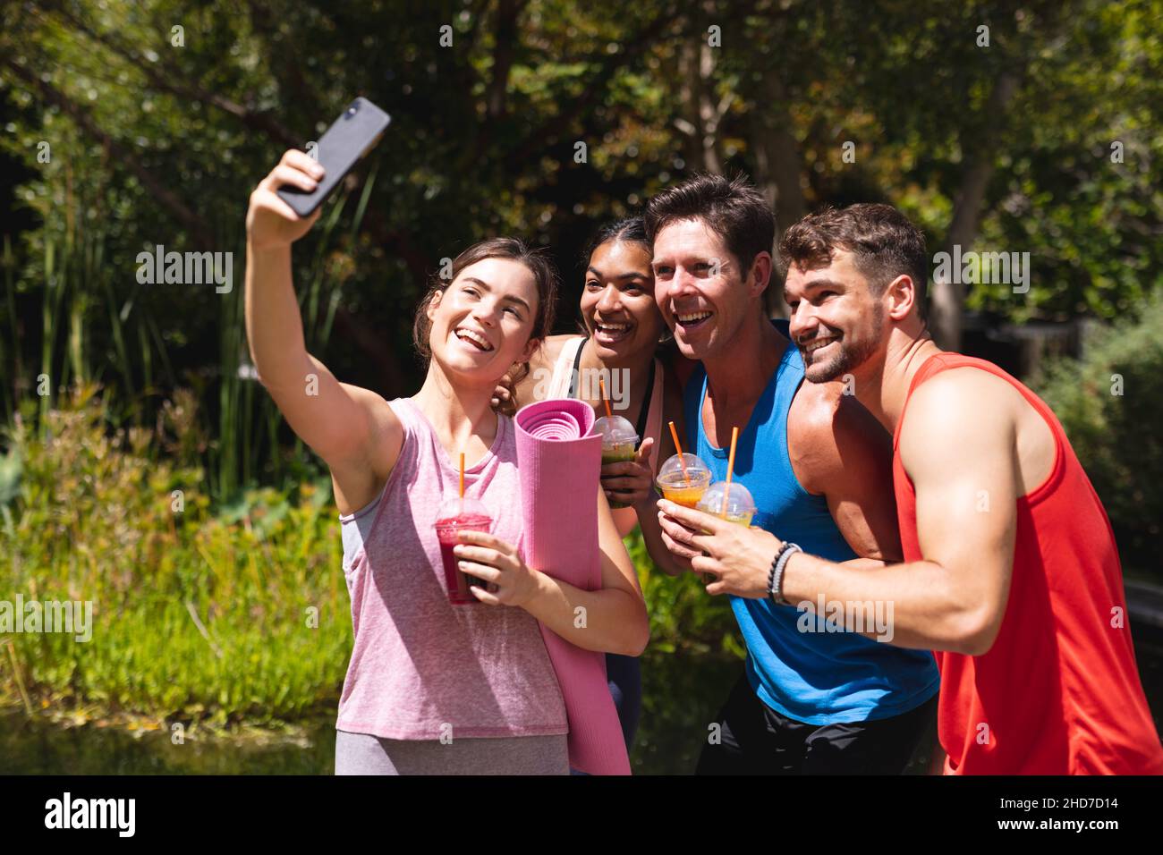 Des amis hommes et femmes heureux prenant le selfie tout en tenant des boissons saines après l'entraînement dans le parc Banque D'Images